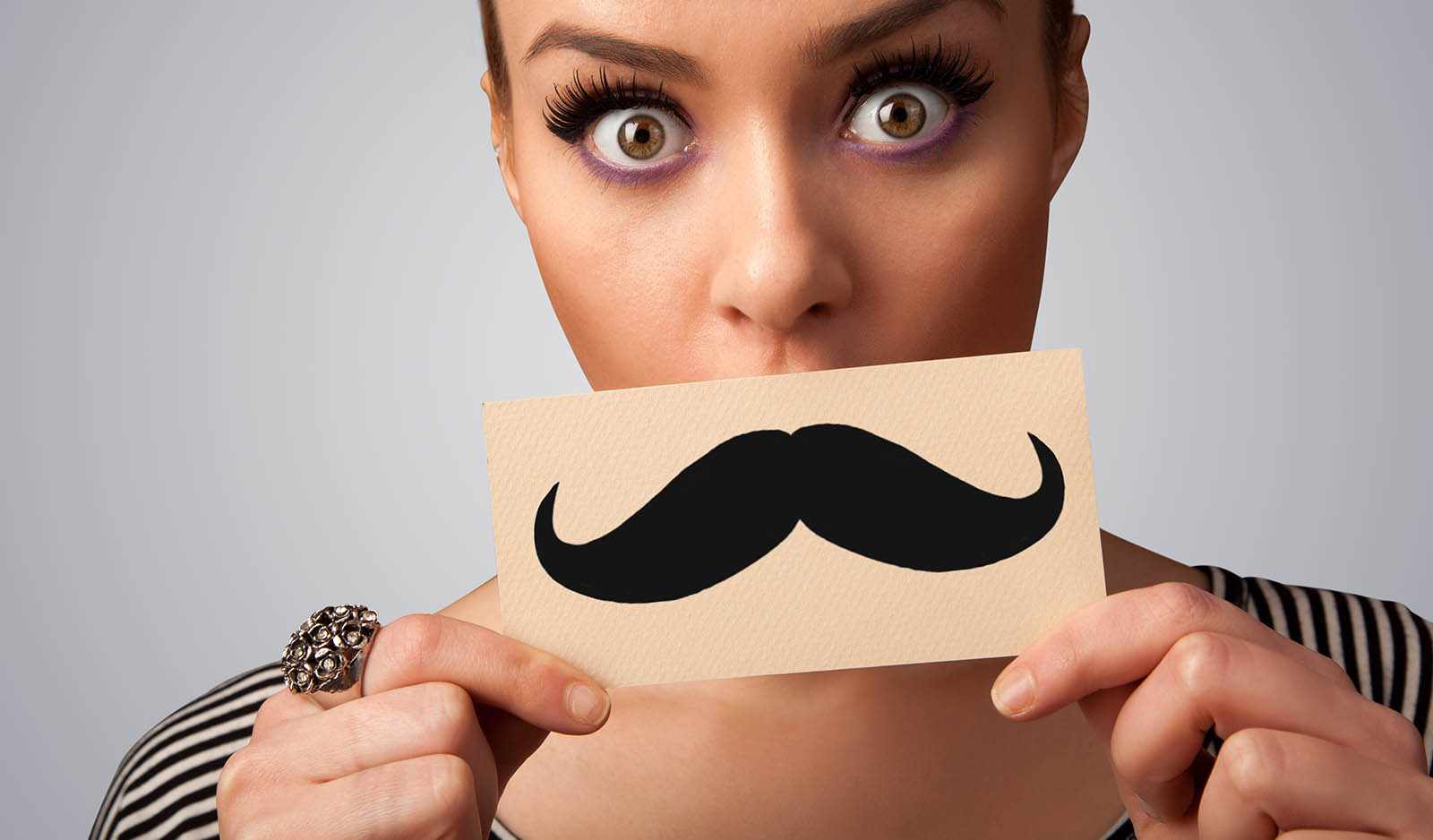 A woman holding up a card with a mustache on it.