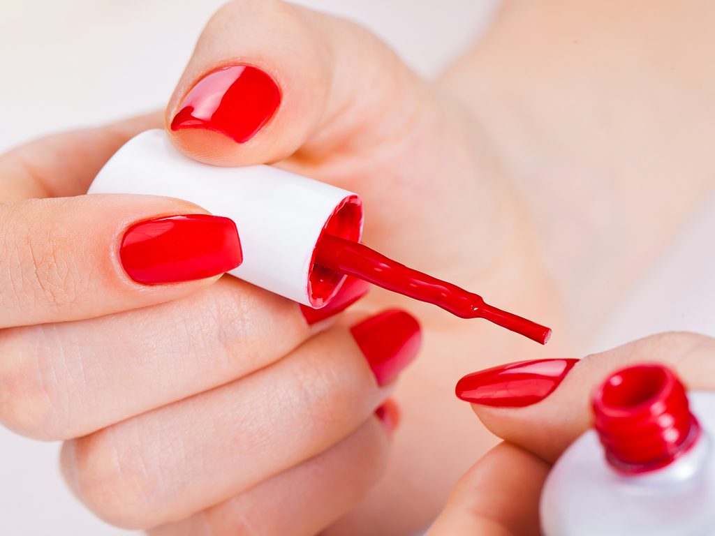 A woman is putting red nail polish on her nails.